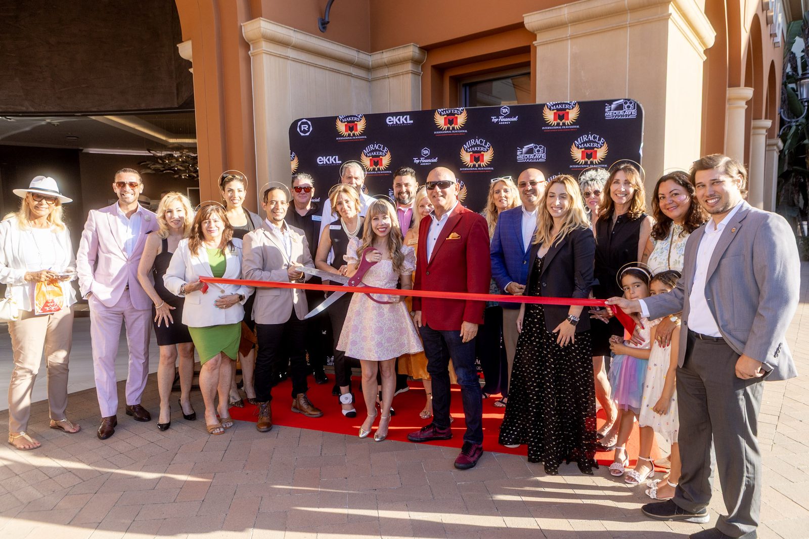 The Miracle Makers team holding the red ribbon across the carpet before the cut